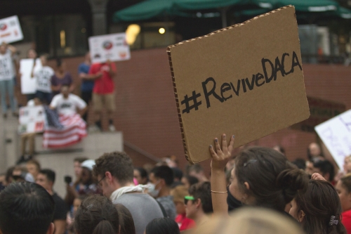A cardboard protest sign with #RevivieDACA written in permanent marker is the only thing in focus amid a crowd of people
