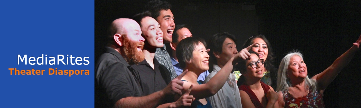 A group of Asian actors stand on the stage looking and pointing to the side
